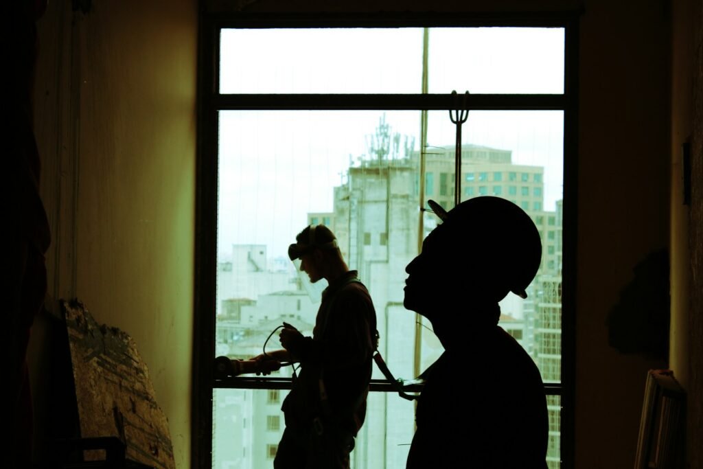 ongoing maintennace being performed by two men wearing hard hat standing near clear glass window