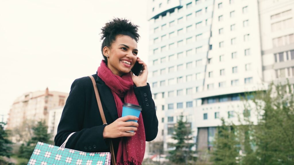 Woman talking on phone holding coffee cup and bag